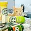 Orange cat next to several Meowijuana products, including Honeysuckle Haze, looking relaxed.